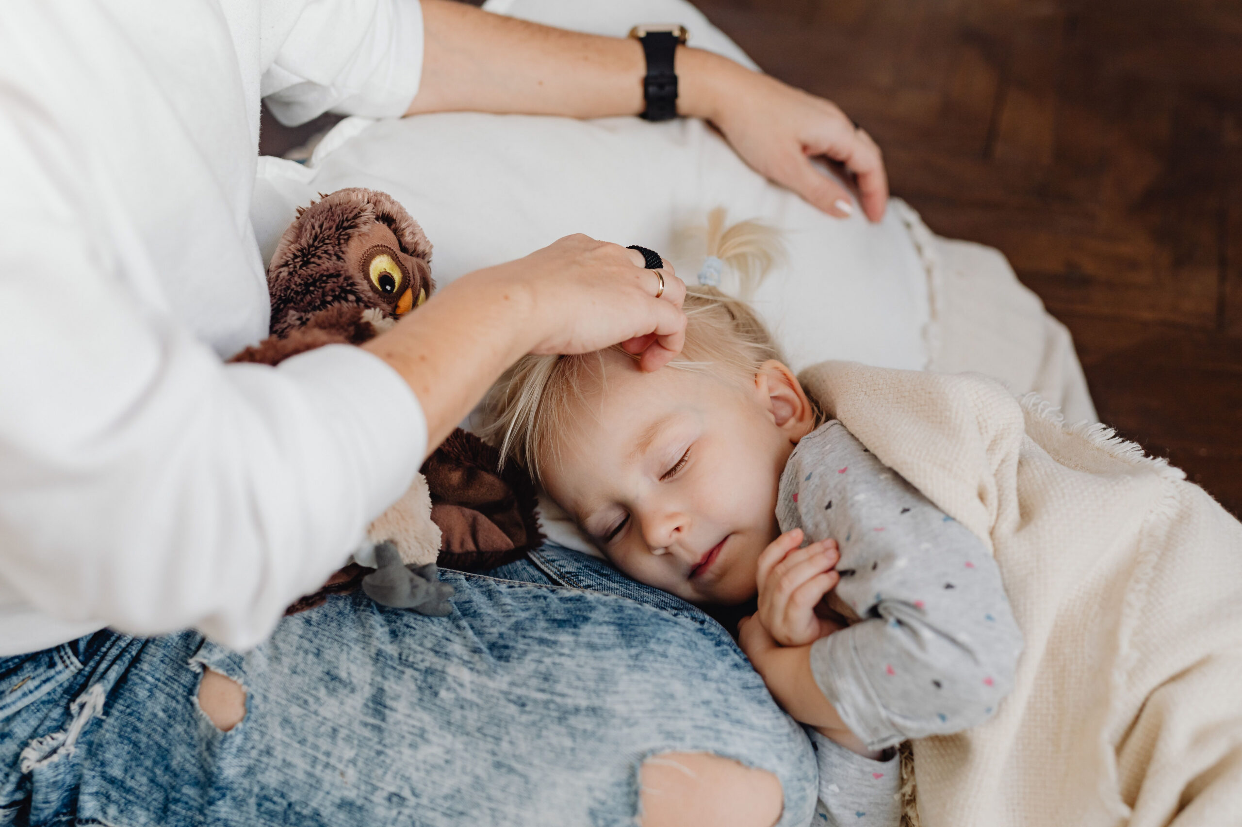 A young child rests on a caregiver’s lap while the caregiver strokes their hair.